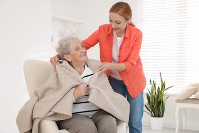 Photo of Caregiver covering senior woman with blanket at home