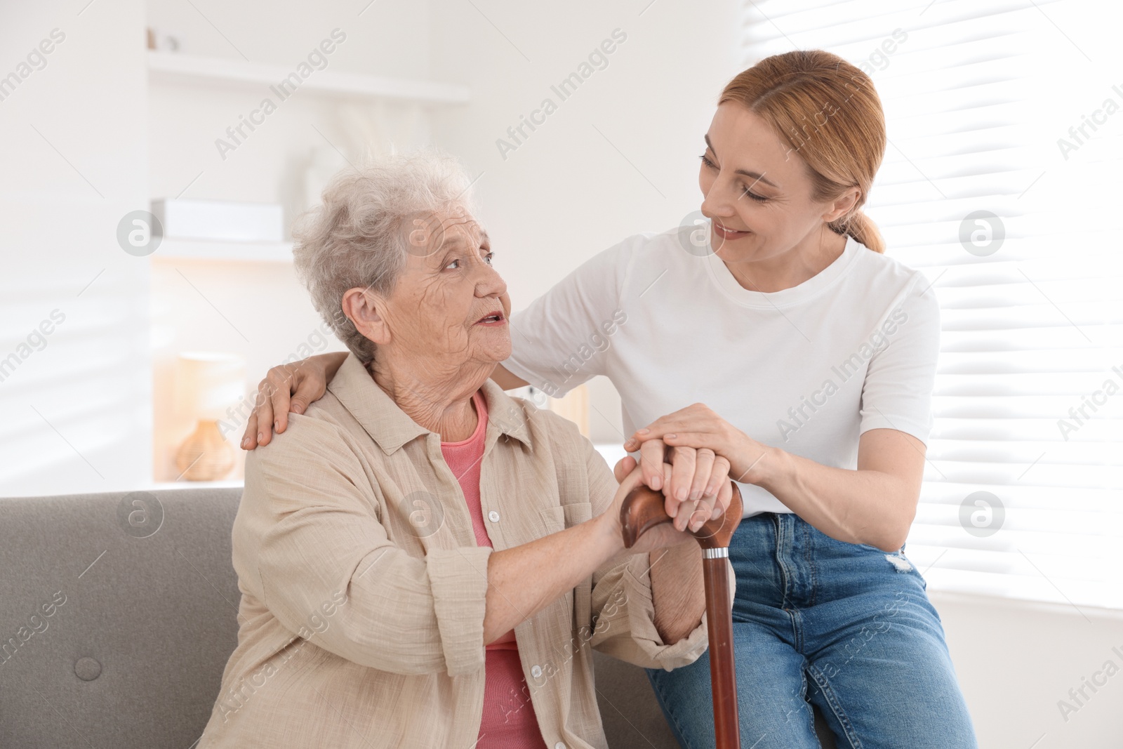 Photo of Caregiver supporting senior woman in living room at home