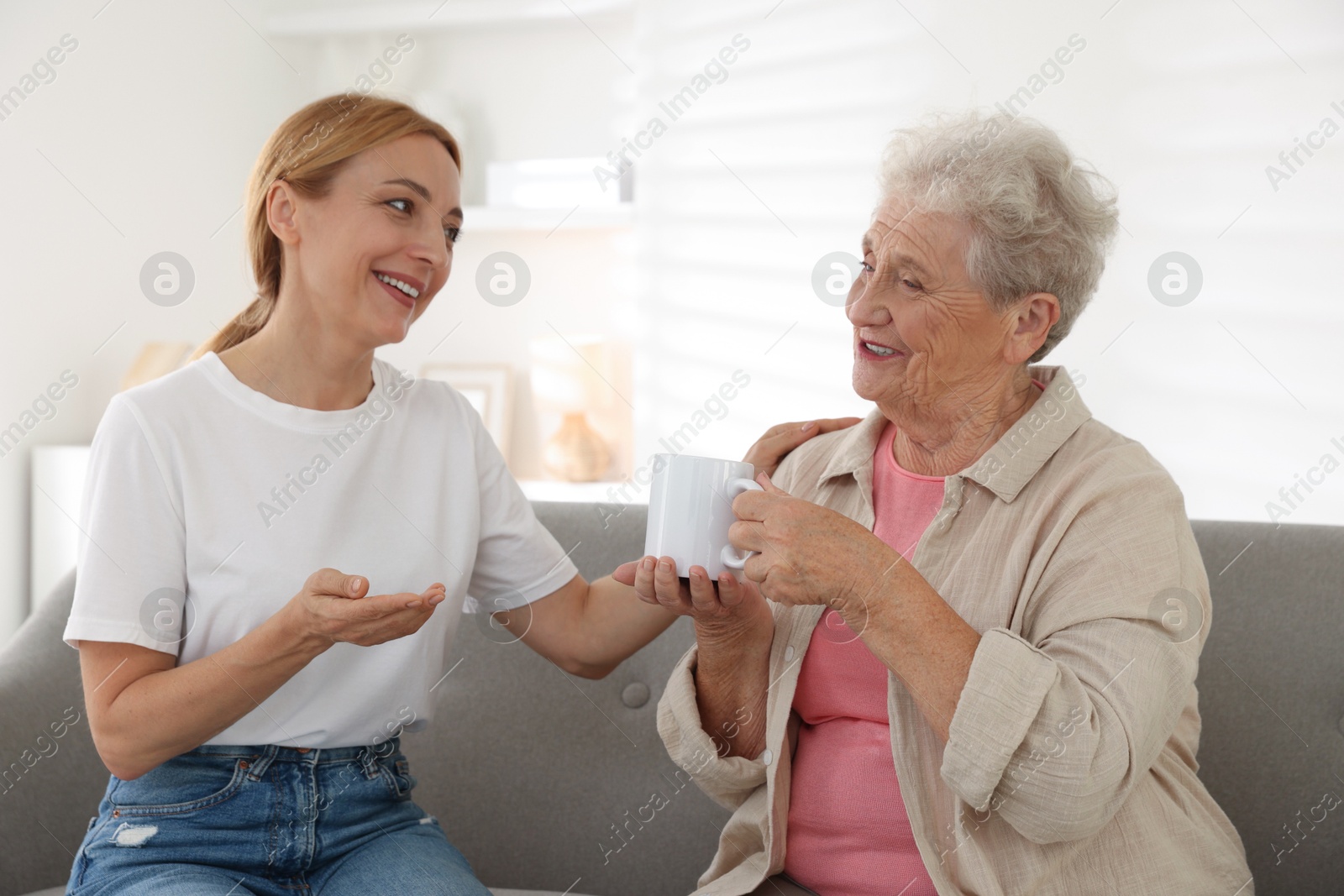 Photo of Caregiver supporting senior woman on sofa at home