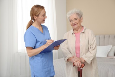 Photo of Healthcare worker with clipboard consulting senior woman indoors