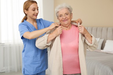 Photo of Healthcare worker helping senior woman to put on jacket at home