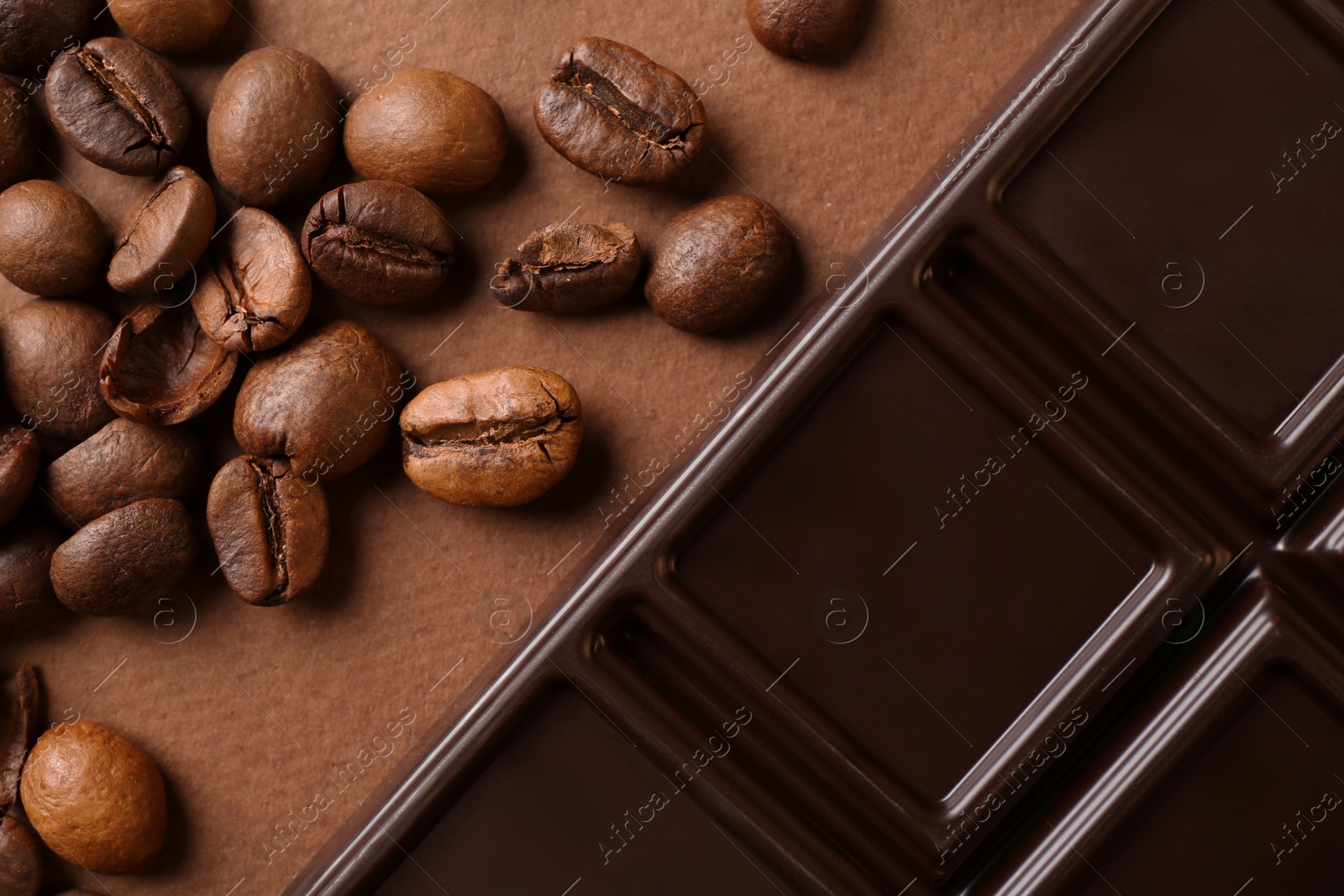 Photo of Tasty chocolate bar and coffee beans on brown background, flat lay