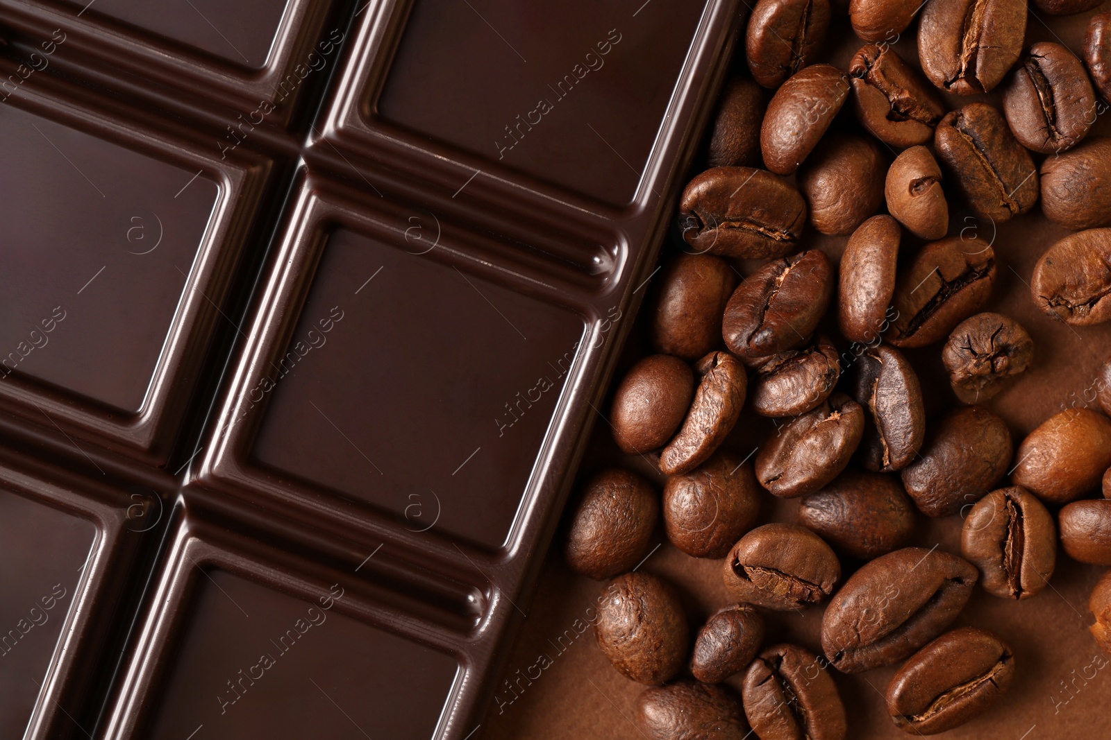 Photo of Tasty chocolate bar and coffee beans on brown background, top view