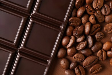 Photo of Tasty chocolate bar and coffee beans on brown background, top view