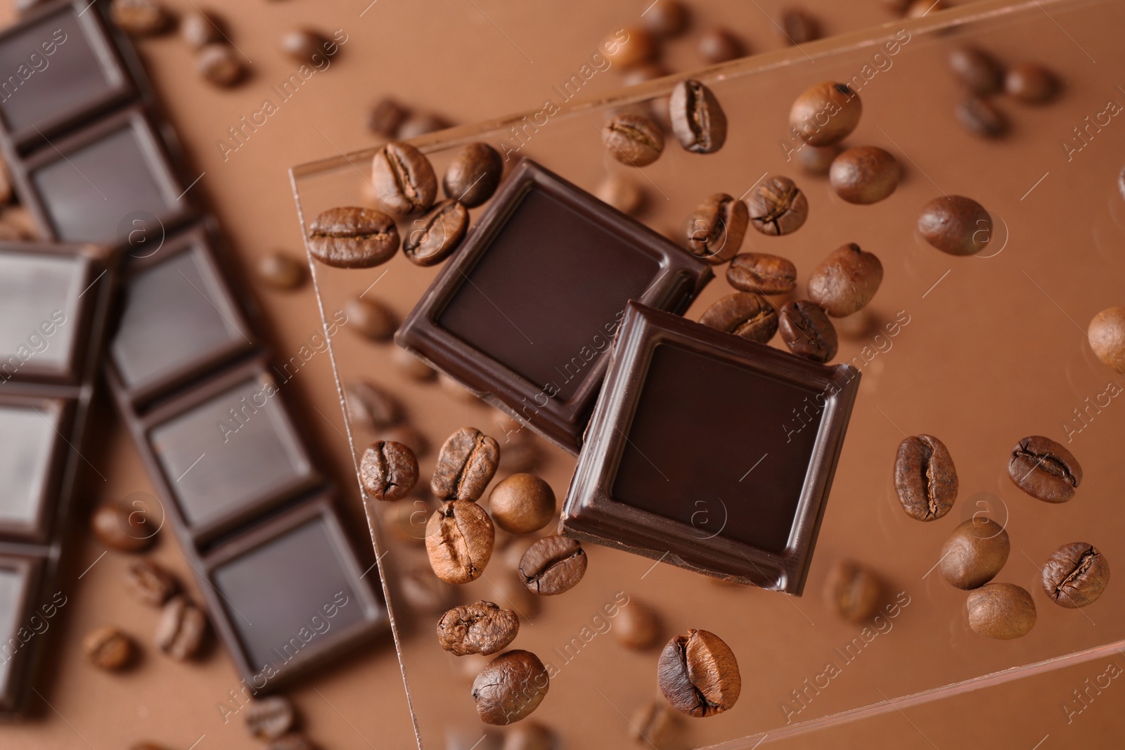 Photo of Pieces of tasty chocolate and coffee beans on glass surface against brown background, top view