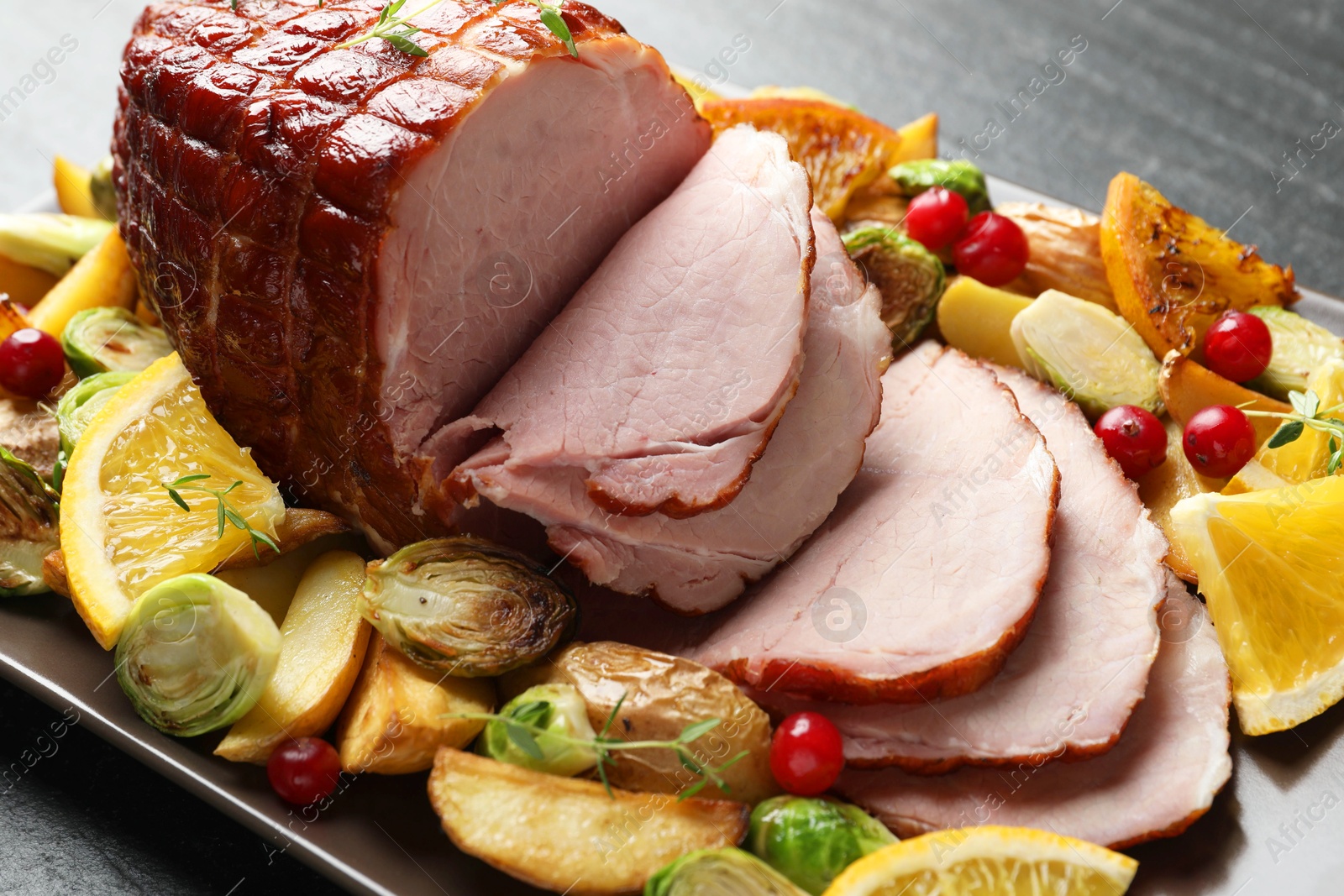 Photo of Tasty baked ham served with vegetables and oranges on black table, closeup