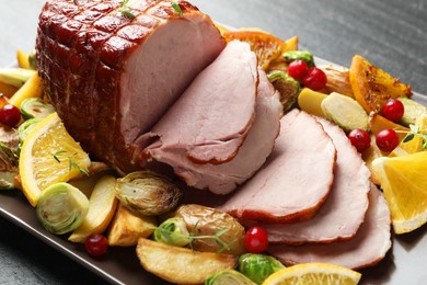 Tasty baked ham served with vegetables and oranges on black table, closeup