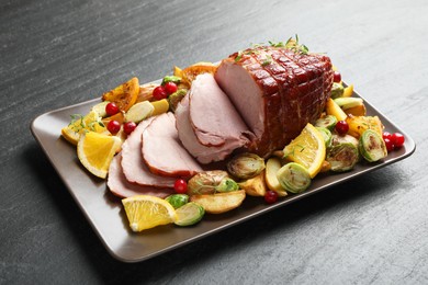 Tasty baked ham served with vegetables and oranges on black table