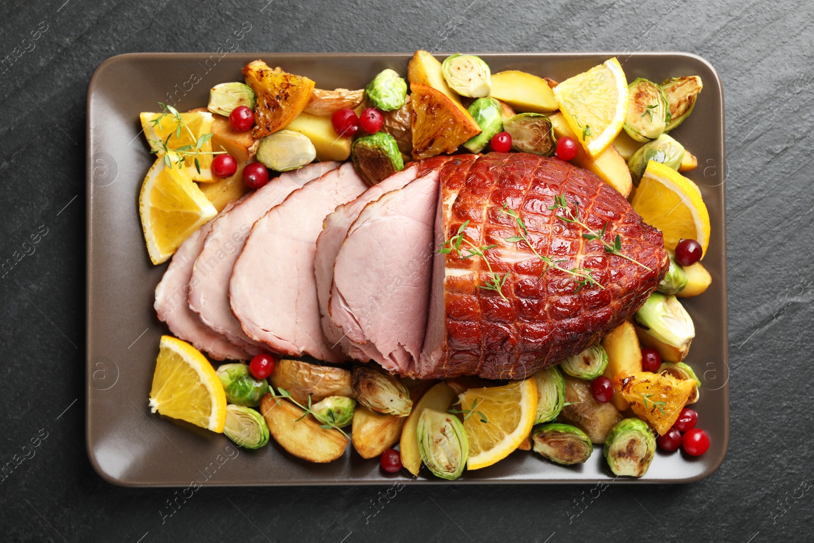 Photo of Tasty baked ham served with vegetables and oranges on black table, top view