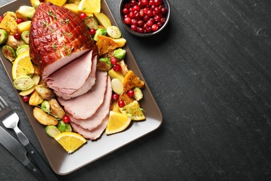 Tasty baked ham served with vegetables and oranges on black table, flat lay. Space for text