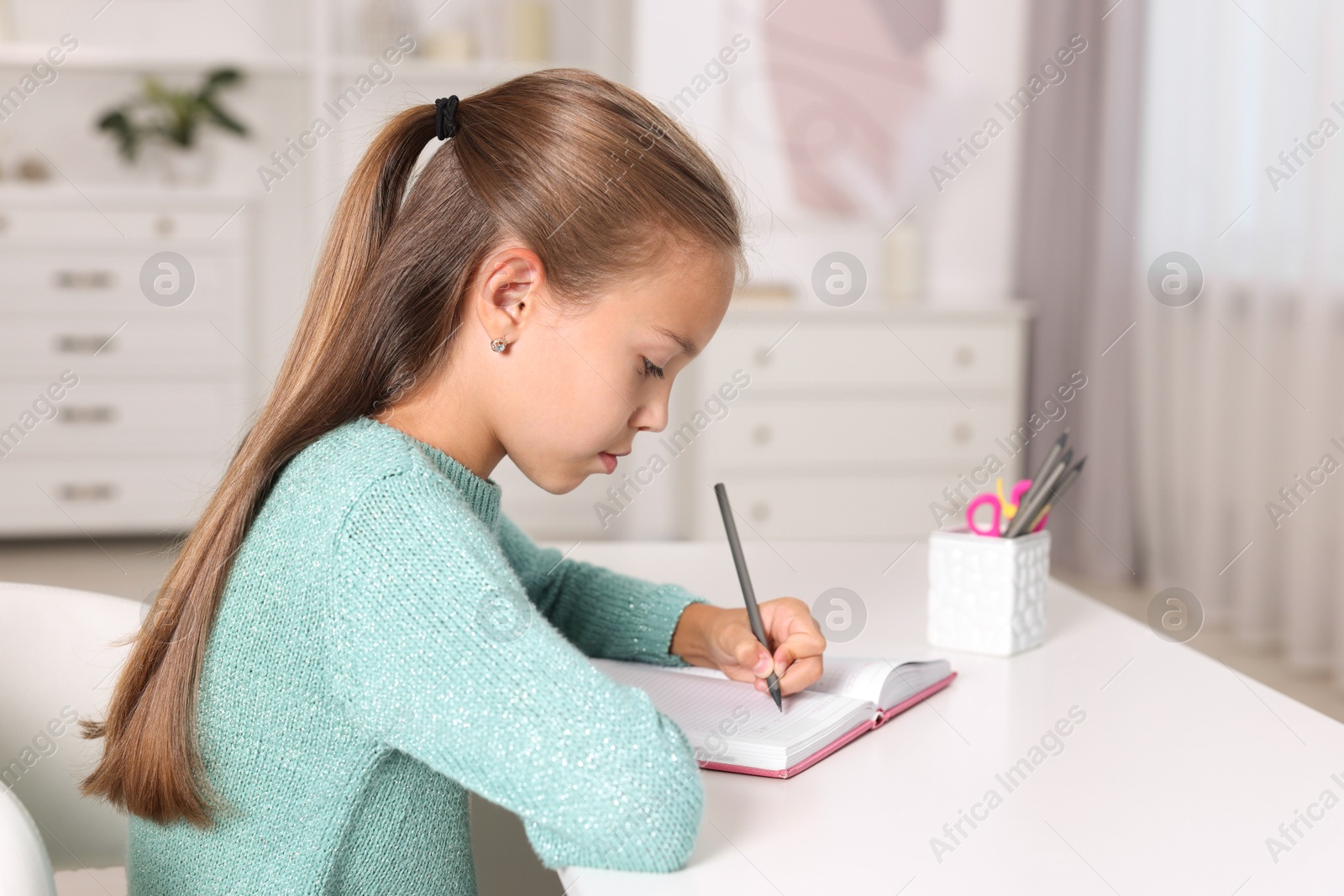 Photo of Girl with incorrect posture doing homework at white desk indoors