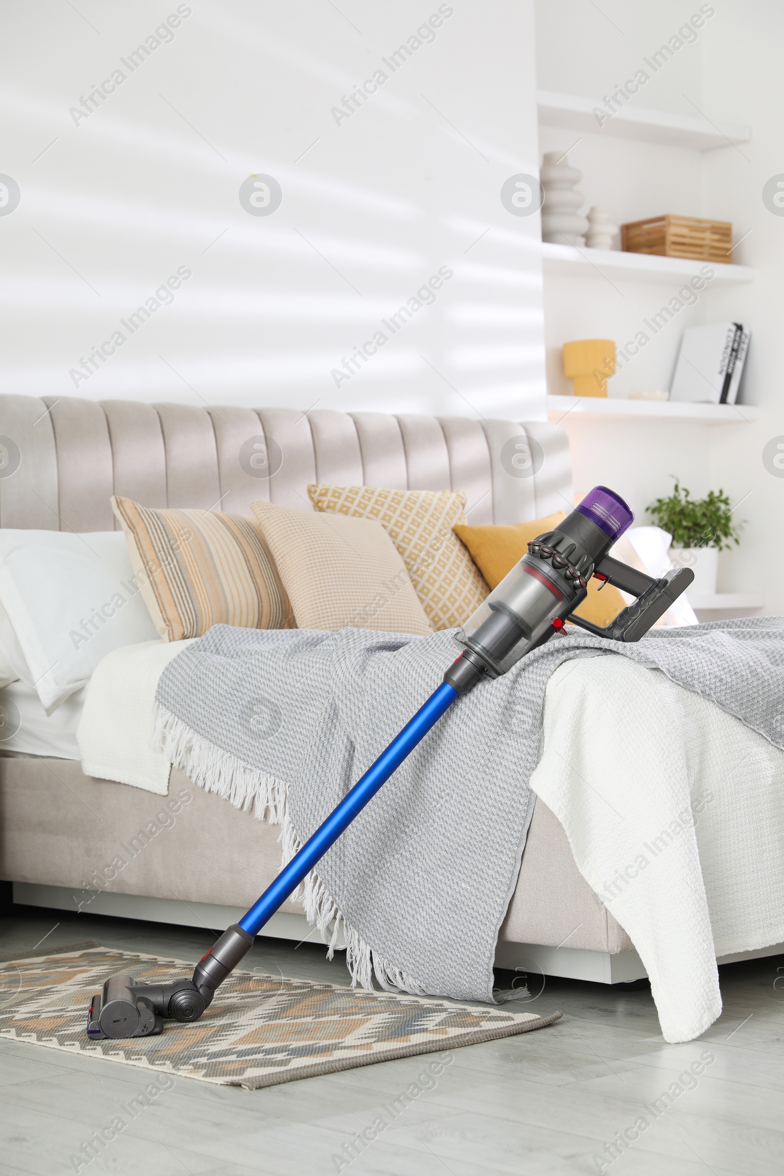 Photo of One cordless vacuum cleaner leaning on bed indoors