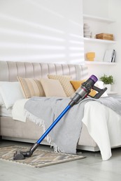 Photo of One cordless vacuum cleaner leaning on bed indoors