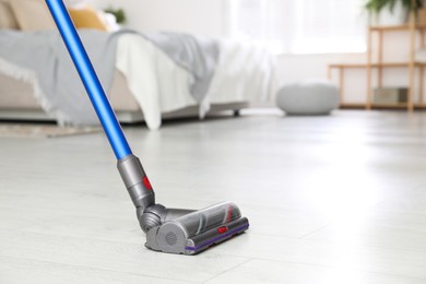 Photo of Cleaning floor with cordless vacuum cleaner indoors, closeup. Space for text