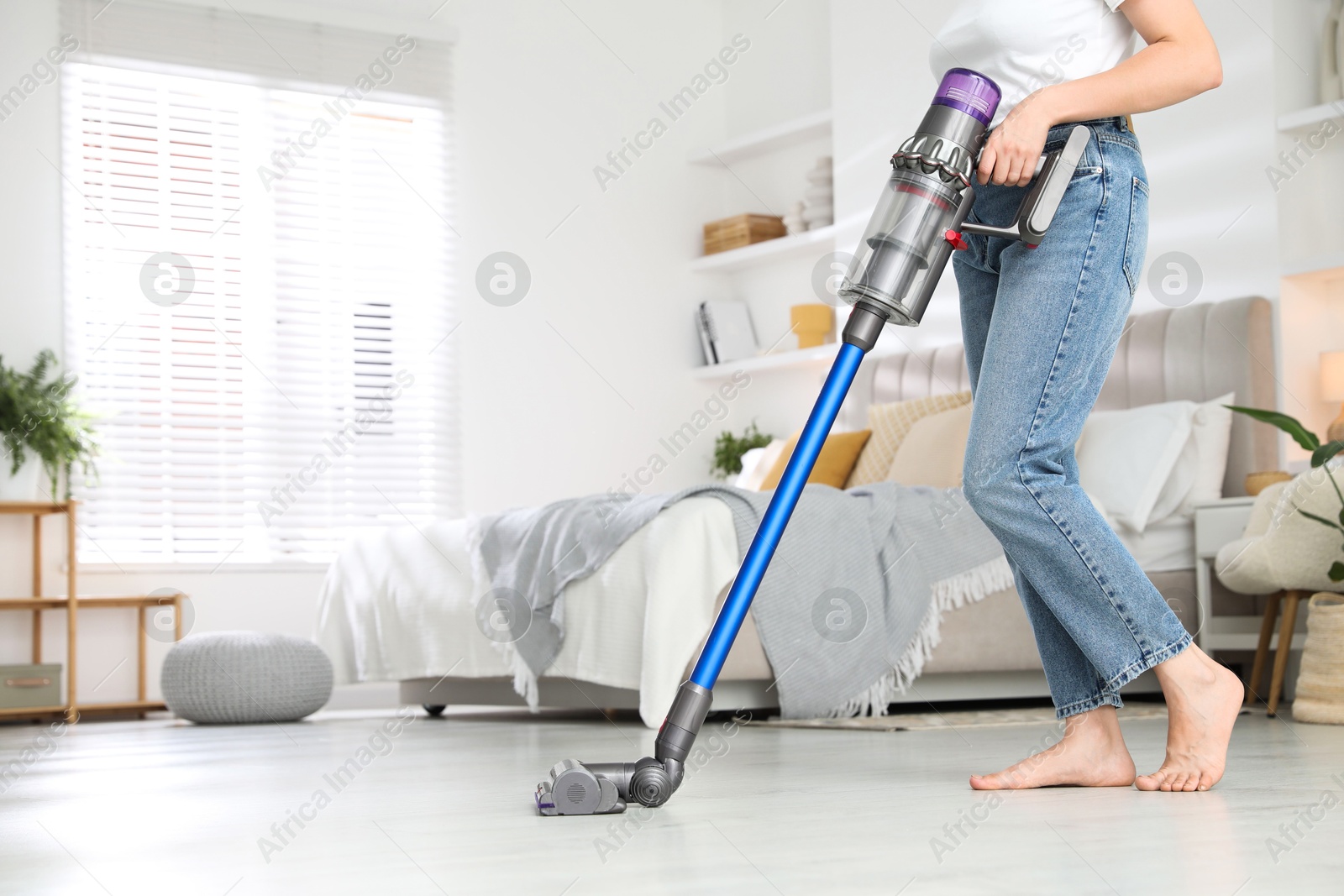 Photo of Woman cleaning floor with cordless vacuum cleaner indoors, closeup. Space for text