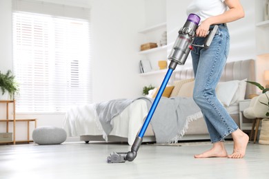 Photo of Woman cleaning floor with cordless vacuum cleaner indoors, closeup. Space for text