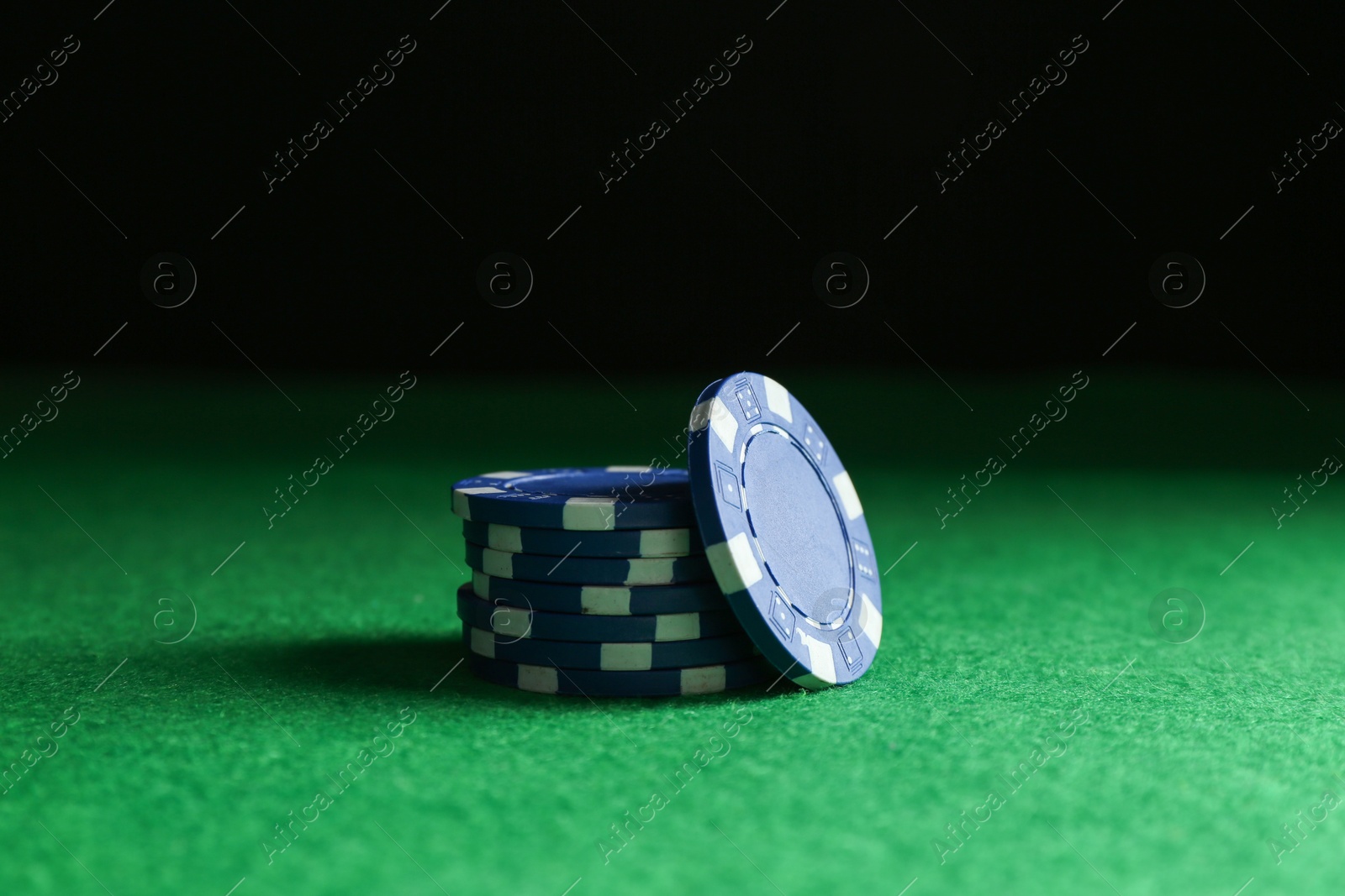 Photo of Stack of poker chips on green table against dark background, closeup