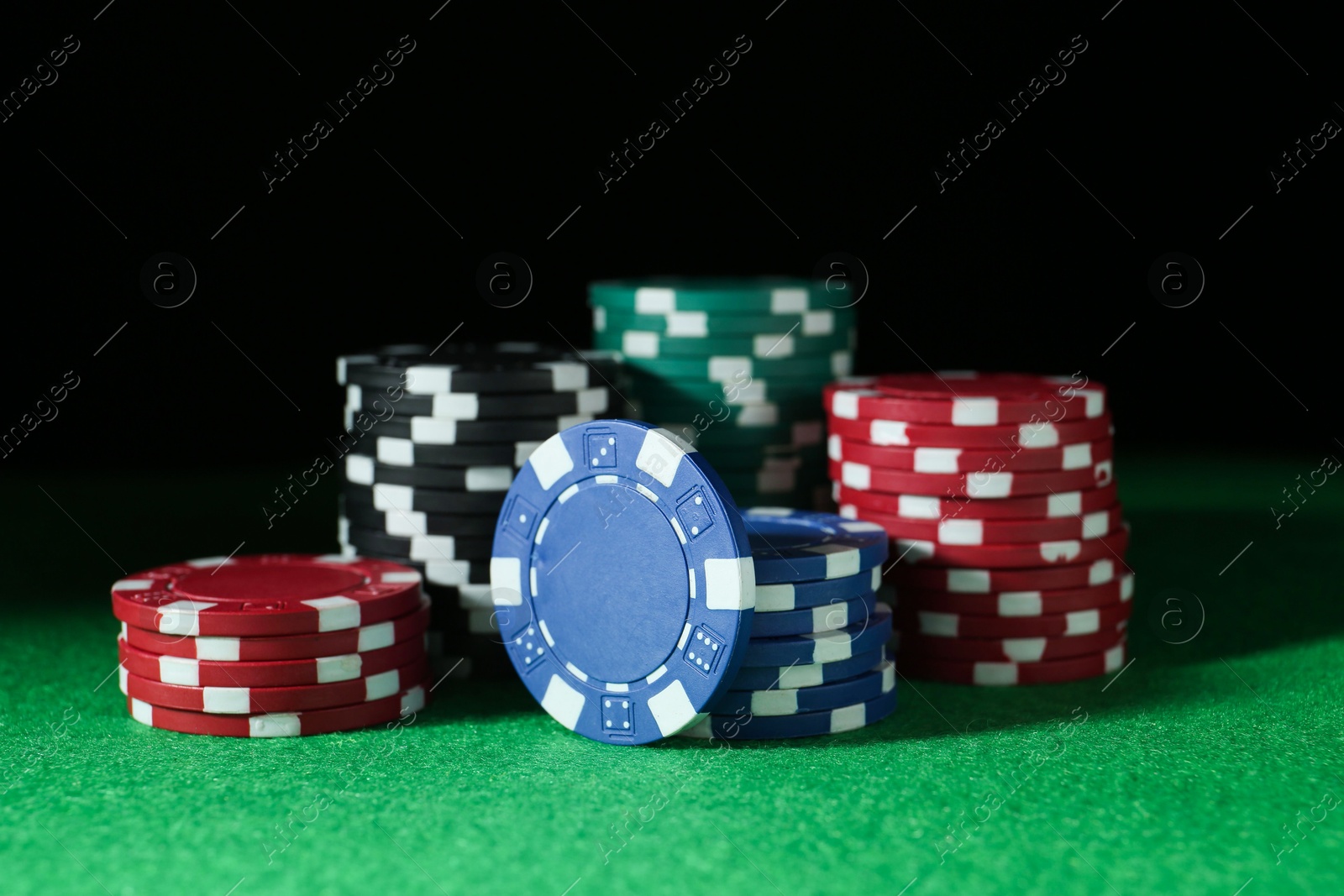 Photo of Poker chips on green table against dark background, closeup