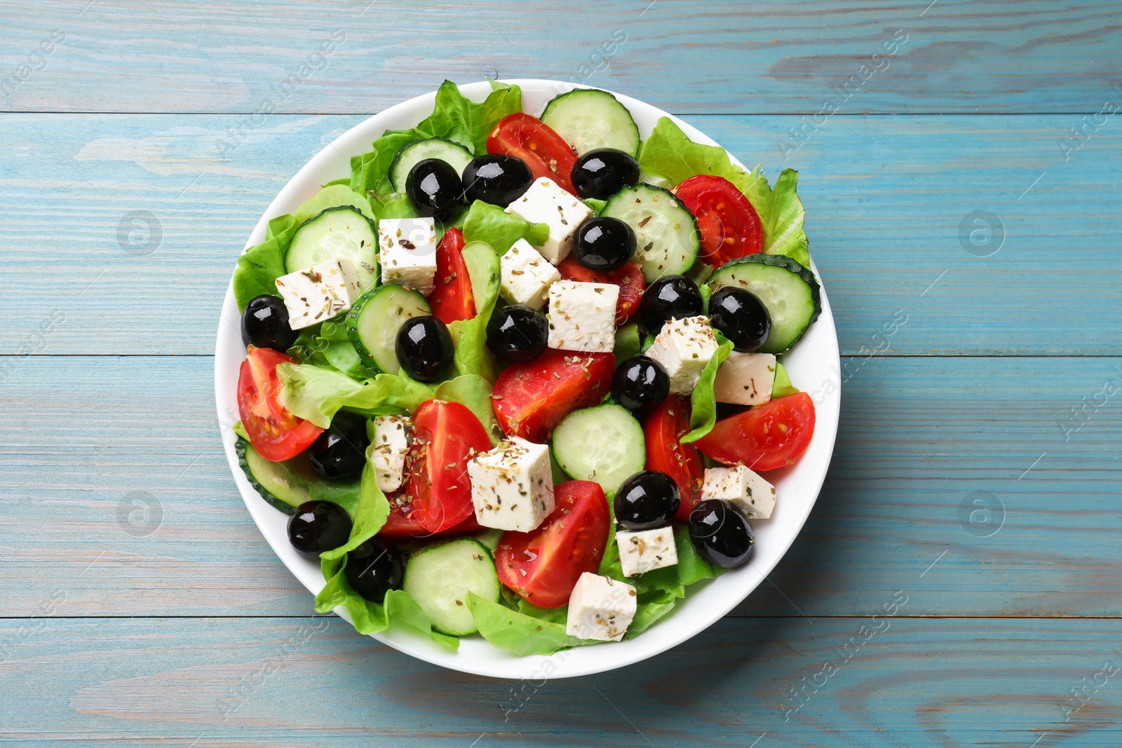 Photo of Delicious salad with feta cheese on light blue wooden table, top view