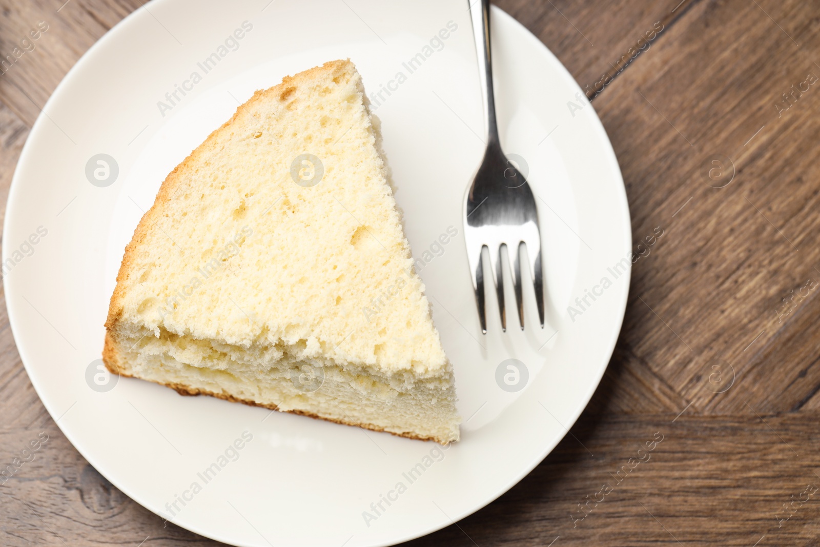 Photo of Piece of delicious sponge cake and fork on wooden table, top view