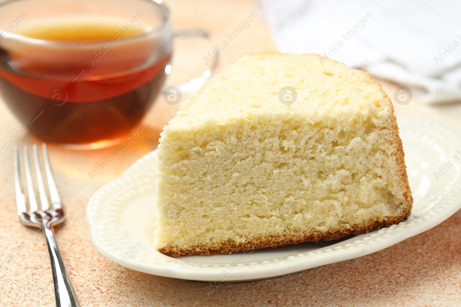 Photo of Piece of delicious sponge cake served on beige textured table, closeup