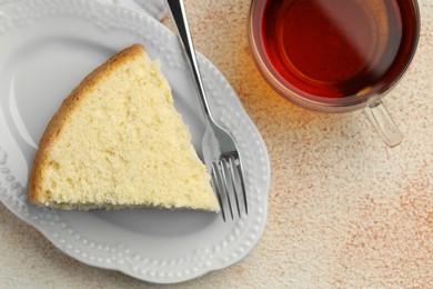 Photo of Piece of delicious sponge cake served on beige textured table, flat lay