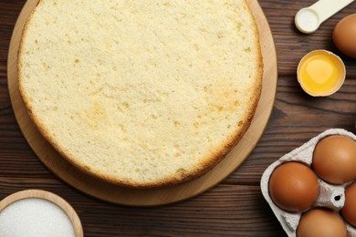 Photo of Delicious cut sponge cake and ingredients on wooden table, flat lay