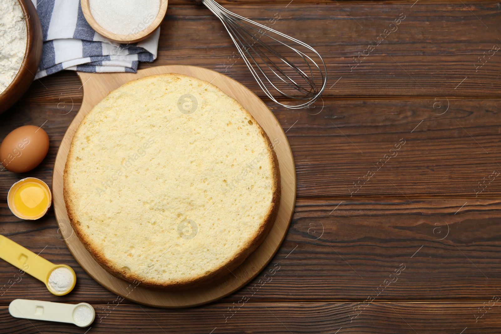 Photo of Delicious cut sponge cake, whisk and ingredients on wooden table, flat lay. Space for text