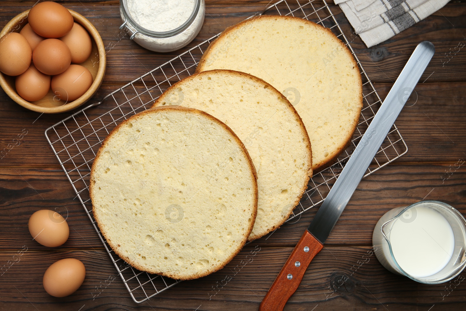 Photo of Delicious cut sponge cake, knife and ingredients on wooden table, flat lay