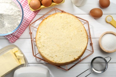 Photo of Delicious cut sponge cake and ingredients on white wooden table, flat lay