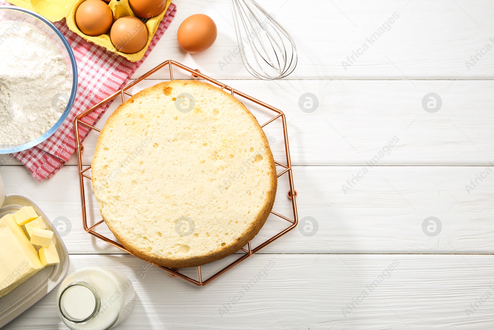 Photo of Delicious cut sponge cake and ingredients on white wooden table, flat lay. Space for text