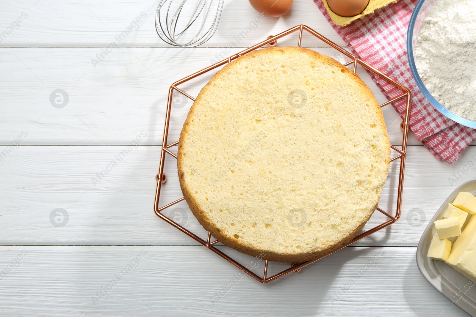 Photo of Delicious cut sponge cake and ingredients on white wooden table, flat lay. Space for text