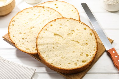 Photo of Delicious cut sponge cake and knife on white wooden table