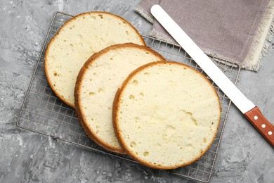 Photo of Delicious cut sponge cake and knife on grey textured table, flat lay