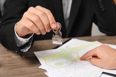 Photo of Real estate agent with house key at wooden table, closeup