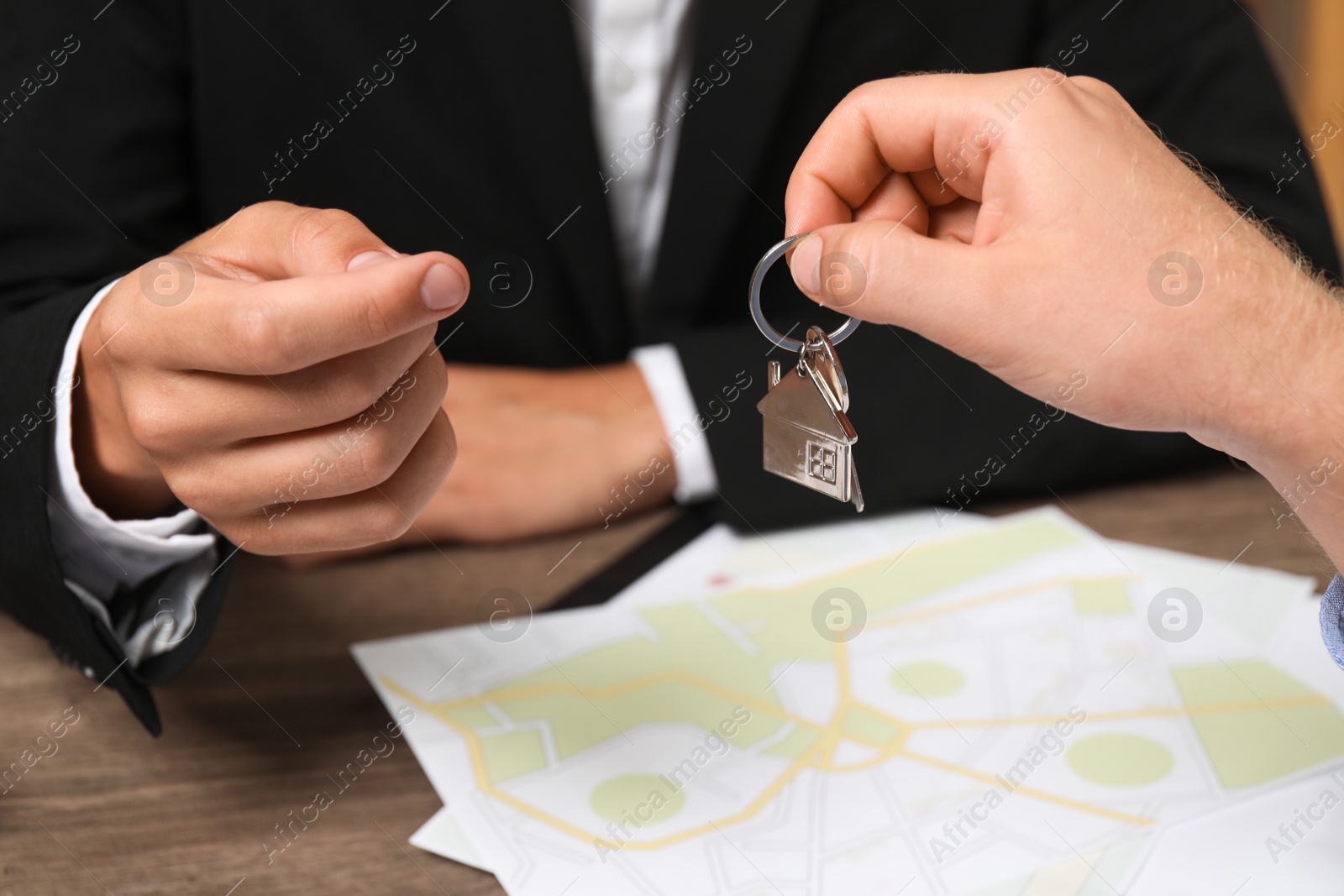 Photo of Real estate agent giving house key to new owner at wooden table, closeup