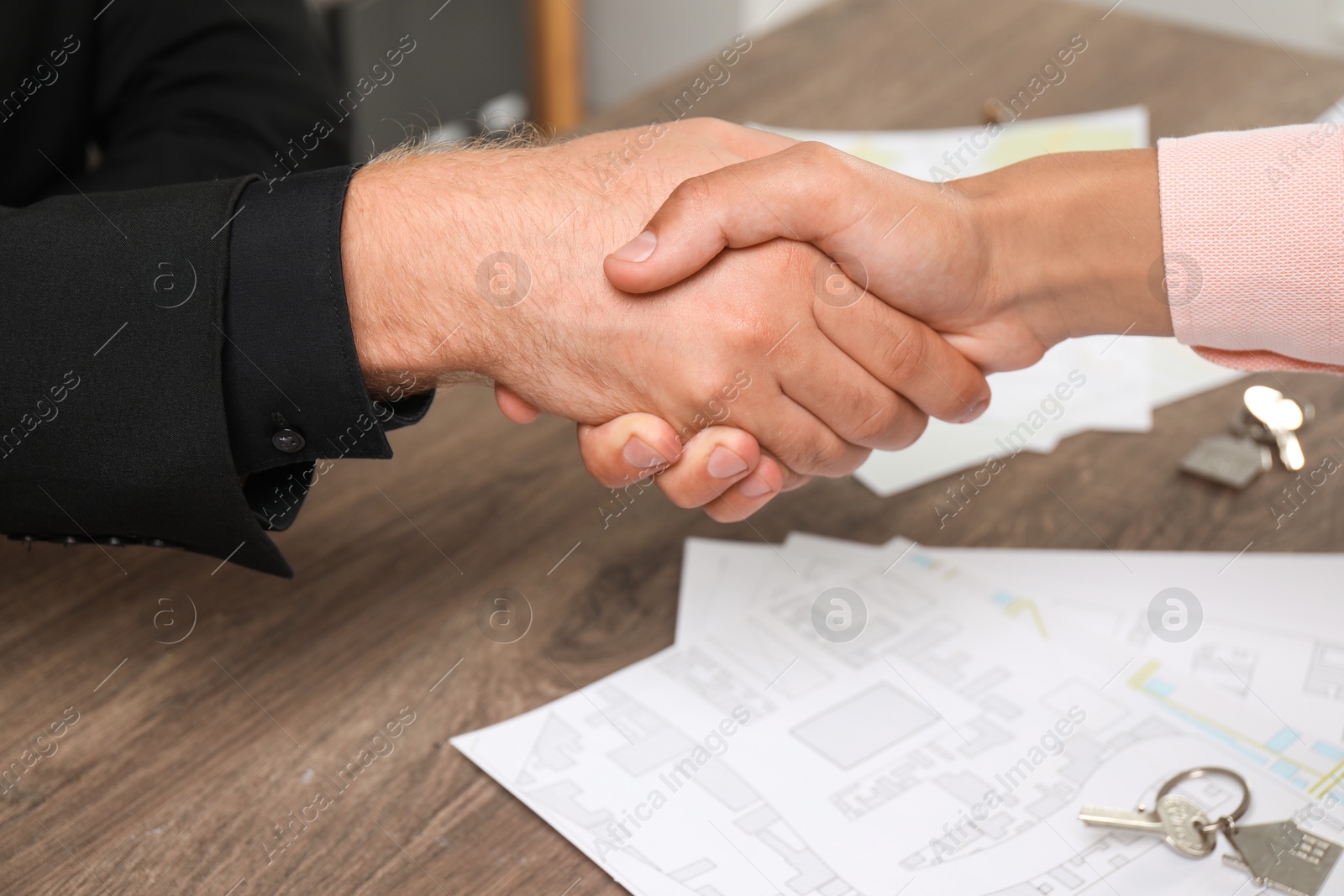 Photo of Real estate agent shaking hands with client at wooden table, closeup