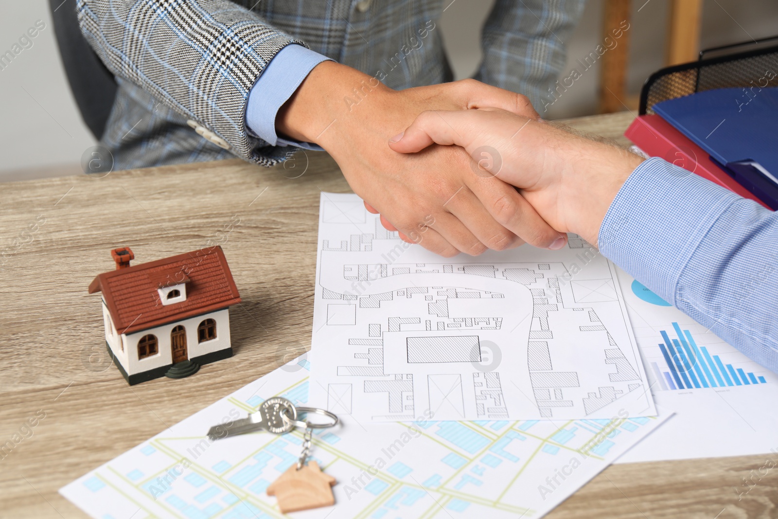 Photo of Real estate agent shaking hands with client at wooden table, closeup