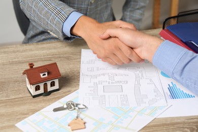 Real estate agent shaking hands with client at wooden table, closeup