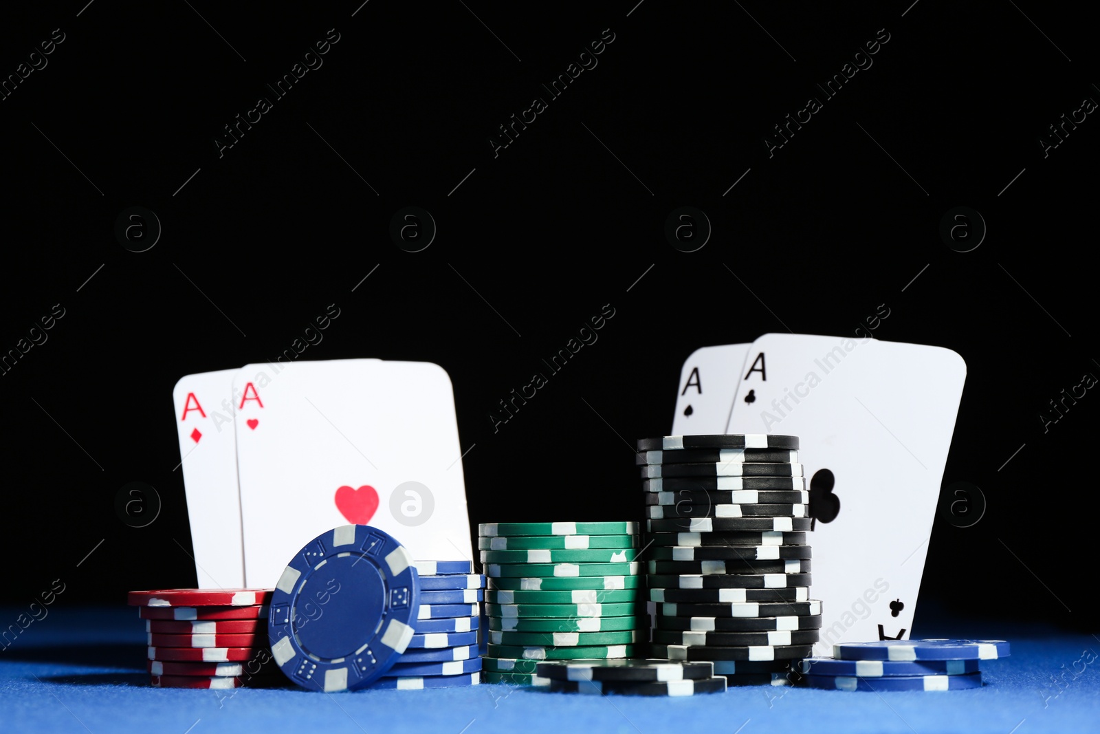 Photo of Playing cards and poker chips on blue table against dark background