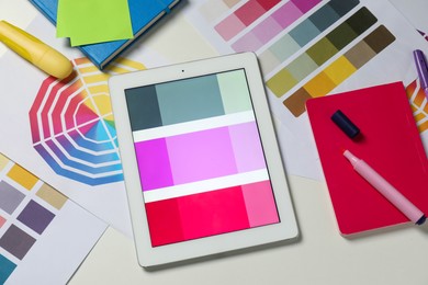 Photo of Designer's workplace with tablet, different palettes and stationery on white table, flat lay