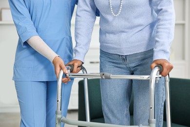 Photo of Nurse helping senior woman with walking frame indoors, closeup