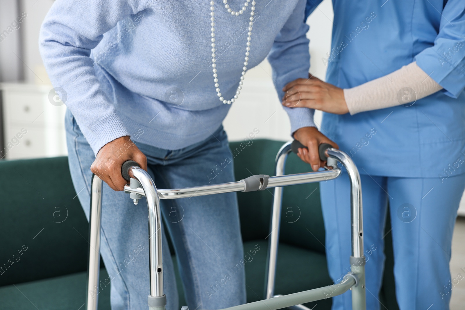 Photo of Nurse helping senior woman with walking frame indoors, closeup