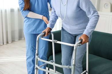 Photo of Nurse helping senior woman with walking frame indoors, closeup