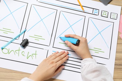 Website designer creating wireframe on paper with highlighter at wooden table, top view