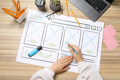 Photo of Website designer creating wireframe on paper with pen at wooden table, top view