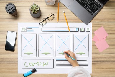 Photo of Website designer creating wireframe on paper with pen at wooden table, top view