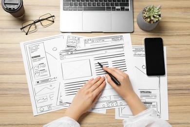 Photo of Website designer creating wireframe on paper with pen at wooden table, top view