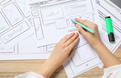 Photo of Website designer creating wireframe on paper with pen at wooden table, top view