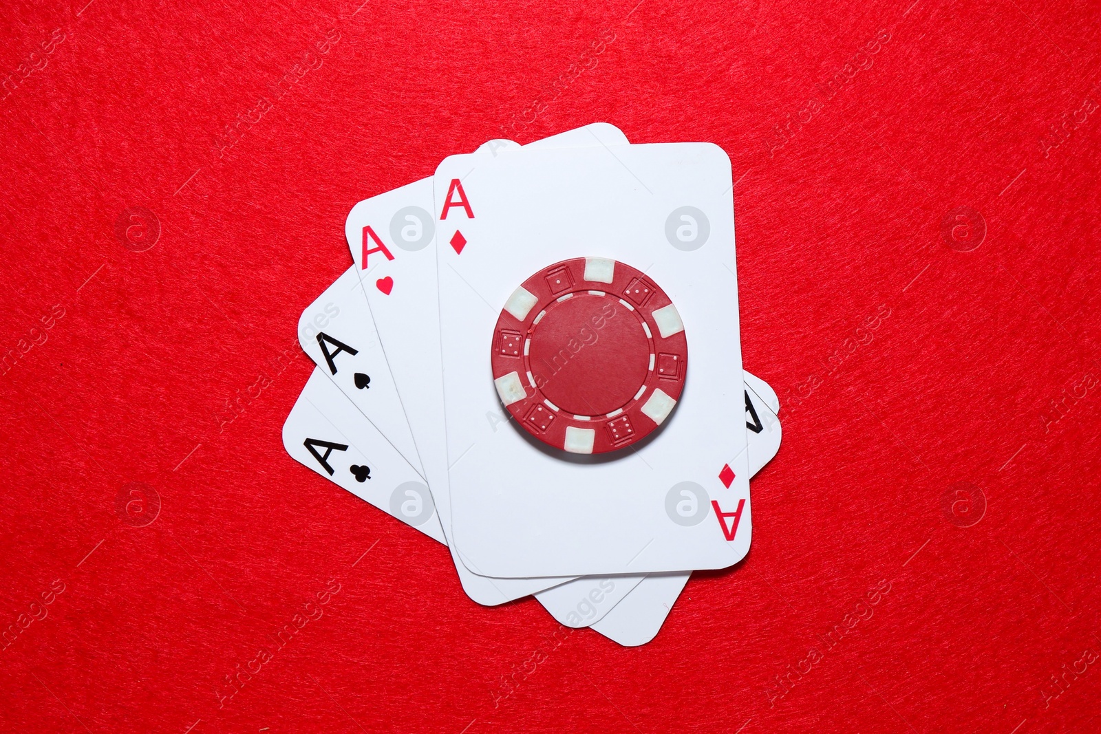 Photo of Playing cards and poker chip on red table, top view